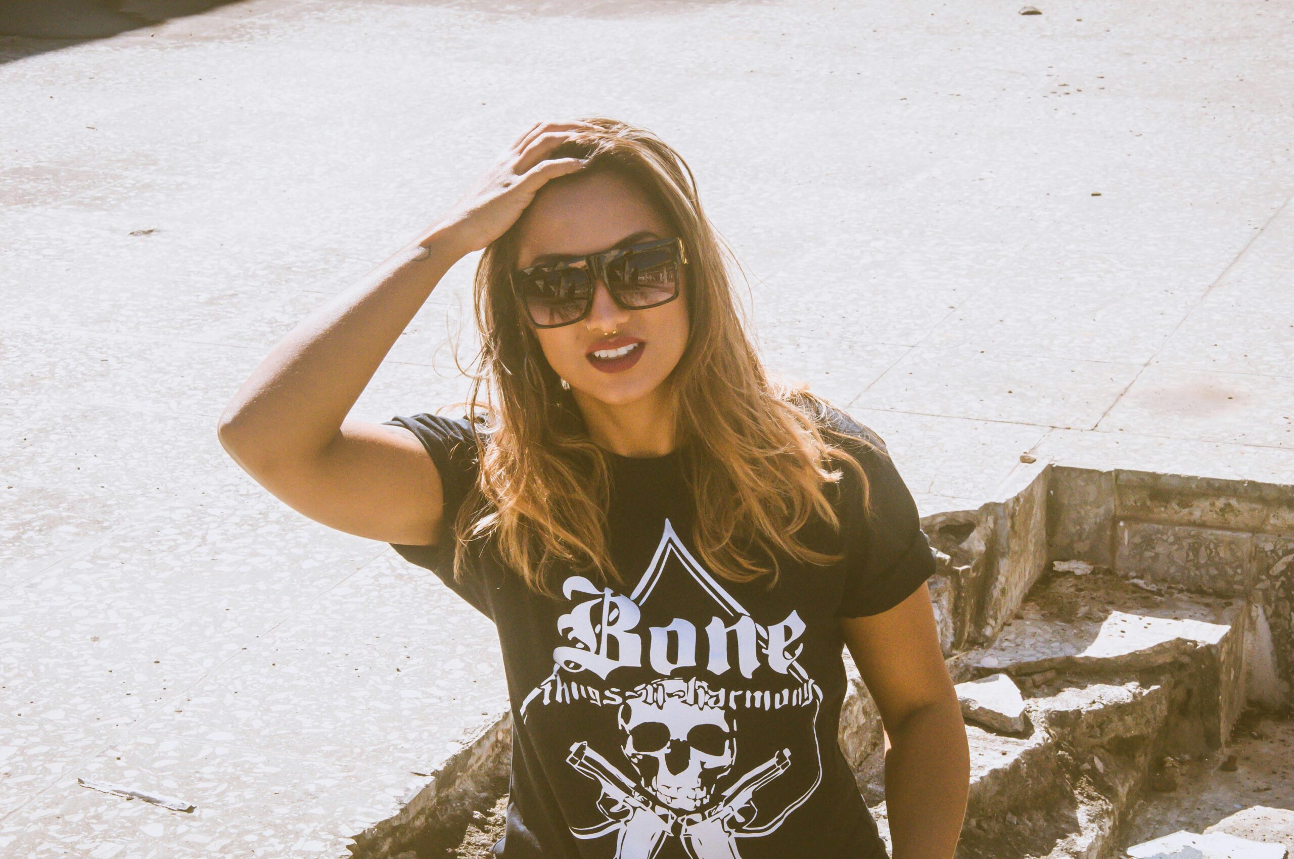 Outdoor portrait of a woman wearing sunglasses and a graphic t-shirt in sunny weather.